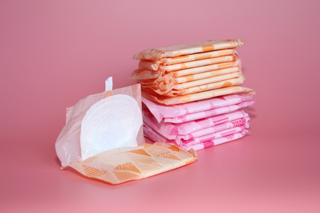 On a rose background are several sanitary pads in individual packaging. One feminine sanitary pad is open.の写真素材