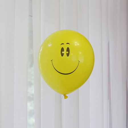 Yellow balloon with a smile. Smiley - a symbol of happiness and joy. Inflatable ball on the background of the window.の写真素材