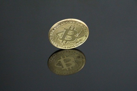 One gold coin bitcoin on a black background. Bitcoin is on its side. One can see his reflection. Cryptocurrency concept gold bitcoin. No people, empty.の写真素材