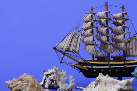 Toy ship on a blue background. Near many seashells. Ship model. Sailboat. Cruise.の写真素材