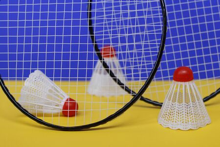 Badminton. Three shuttlecocks and two badminton racket. The colored background is blue and yellow....
