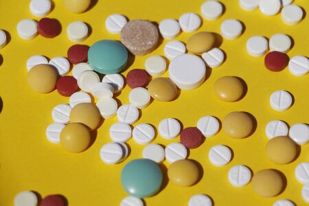 A lot of multi-colored pills on a yellow background. The tablets are scattered. The medicine. Treatment concept.の写真素材