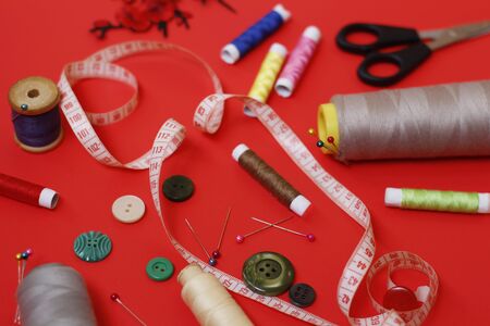 Composition with threads and sewing accessories on a red background. Sewing supplies and needlework accessories. Spools of thread, scissors and needles on a red background.の写真素材