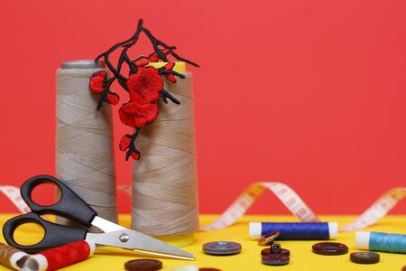 Two large spools of thread are standing, many small spools are lying. Large scissors for sewing, but the photo has buttons and a measuring tape. Needlework concept. Bright background.の写真素材