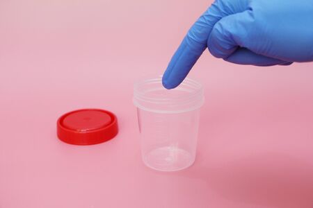Doctors finger points to an empty urine collection jar. Transparent jar for collecting analyzes. The medicine. Urine plastic container with red lid. Concept. It is necessary to pass medical tests.の写真素材