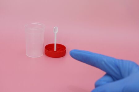 Doctors finger points to an empty can of feces. Transparent jar for collecting analyzes. The medicine. Plastic container with a red lid. The cover is removed. Concept. It is necessary to pass tests.の写真素材