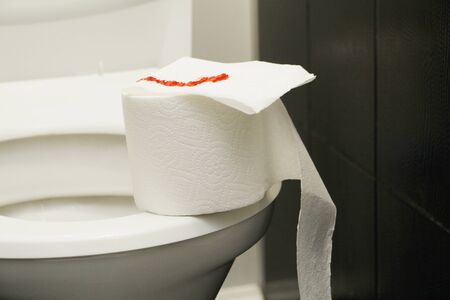 A roll of toilet paper with blood lies on the toilet. The concept of sexual diseases. Blood on toilet paper. Restroom.の写真素材