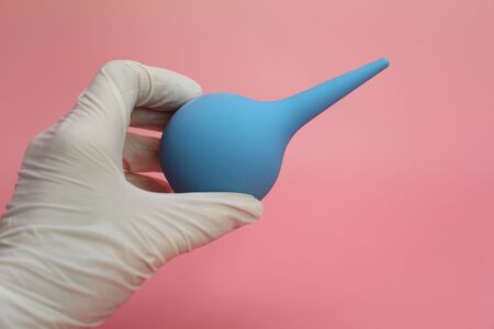 Blue syringe with a soft tip in the female hand of a doctor. A hand in a latex glove holds an enema. The medical enema is blue. The concept of treatment of chronic prostatitis.の写真素材