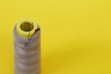 Needlework concept. One large spool of thread and needle on a yellow background. Plenty of room for...