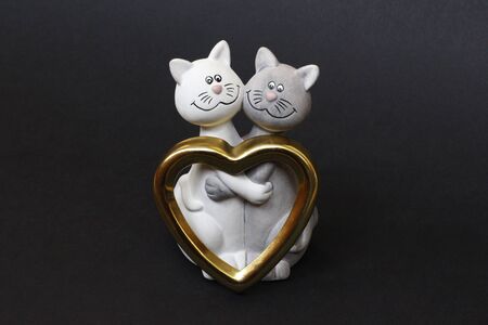 Two cats are hugging. Cats are close and love each other. Valentines Day. Figurine cats in love. Nearby is a golden heart. Cats together are a symbol of lovers. Congratulation.の写真素材
