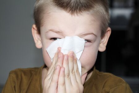 Moscow, FR, 01.26.2019: The boy wipes his nose with a napkin. The child blows his nose. The kid is sick with allergy symptoms. Young cute boy blows his nose in a paper napkin.のeditorial素材
