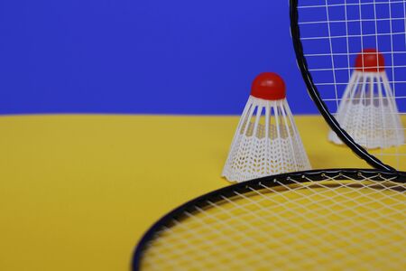 Badminton. Two shuttlecocks and two badminton racket. The colored background is blue and yellow. Idea for a magazine.の写真素材