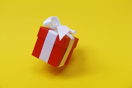 Red gift box with a white bow on a yellow background. The box is closed by a lid. The gift is in the air.の写真素材