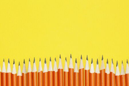 Black lead pencils on a yellow background. Lead pencils. A lot of the same pointed pencils.