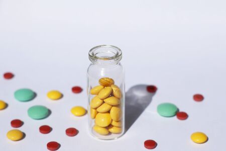 A glass container with prescription medicine is standing, and multi-colored tablets are scattered nearby. Medical theme.の写真素材