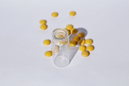 Medical theme. Yellow pills fall out of the bottle. The prescription drug container is on its side, and pills are scattered nearby.の写真素材