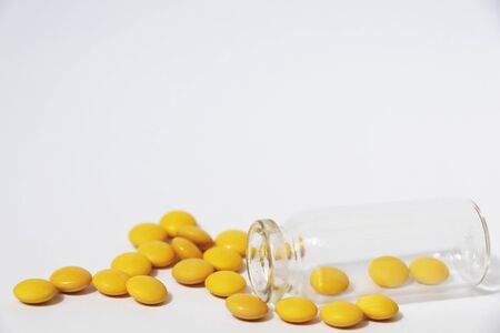 Medical theme. Yellow pills fall out of the bottle. The prescription drug container is on its side, and pills are scattered nearby.の写真素材
