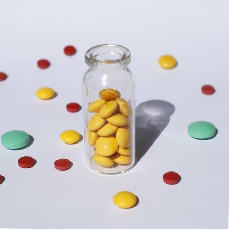 A glass container with prescription medicine is standing, and multi-colored tablets are scattered nearby. Medical theme.の写真素材