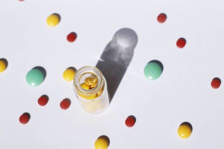 A glass container with prescription medicine is standing, and multi-colored tablets are scattered nearby. Medical theme.の写真素材