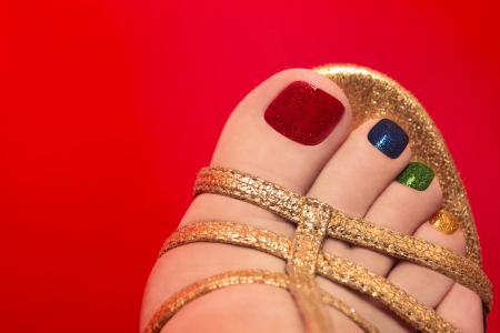 Beautiful multicolored pedicure on female leg on a red background の写真素材