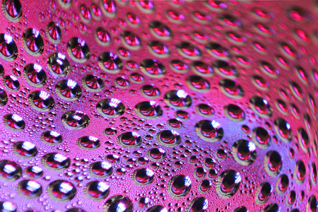 Water drops on color illuminated pink purple surface.の写真素材
