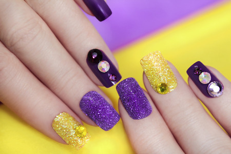Lilac purple manicure with gold glitter and rhinestones in different colors on a purple background.の写真素材