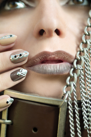 Makeup and manicure in brown and beige shades with a pattern of chains and rhinestones on very oval nails.の写真素材