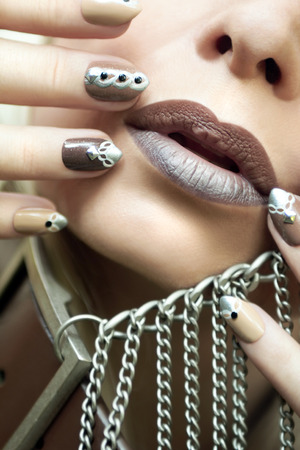 Makeup and manicure in brown and beige shades with a pattern of chains and rhinestones on very oval nails.の写真素材