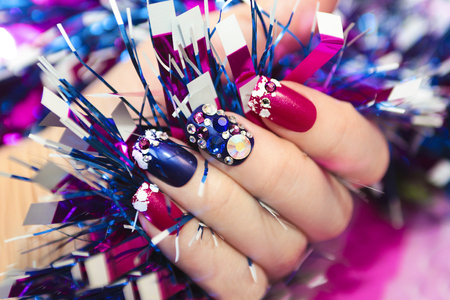 Christmas winter blue manicure with rhinestones of different shapes and sequins in the form of snow on female hand with tinsel.の写真素材