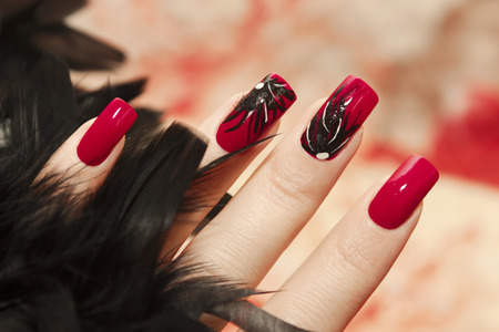 Long red nails with design of black feathers on female hand close up.の写真素材