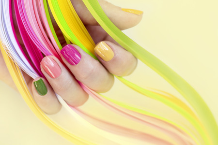 Colorful multi-colored manicure on a short nails on a yellow background. Nail art. Pink, green, yellow, peach nail Polish.の写真素材