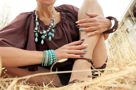 Multi-colored manicure on long oval nails on a woman with brown and blue bracelets on her hands in summer on nature.の写真素材