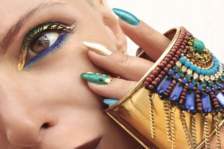 Multi-colored fashionable makeup and manicure in turquoise Golden blue and brown tones. Nail art with metal rhinestones on the nails.の写真素材