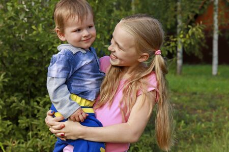 The girl holds a little boy in her arms, they smile together and enjoy life in the summer weather.の写真素材