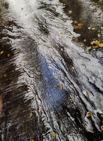 Abstract blur of water with foam along the road surface with fallen leaves in autumn.の写真素材