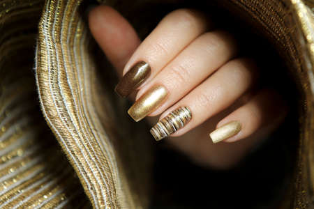 Fashionable manicure with a matte Golden color of nail Polish and brown on a long nail shape.の写真素材