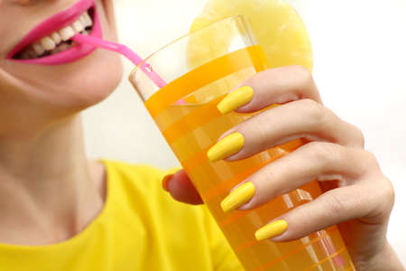 Young woman drinking pineapple juice with joy. Trendy manicure with yellow nail polish on a long form.の写真素材