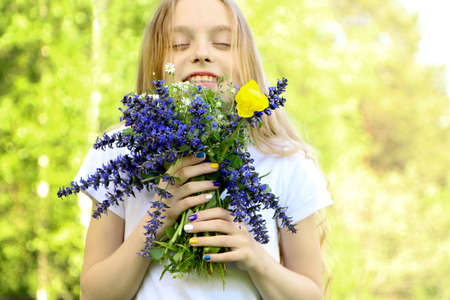 Beautiful blonde girl holding a bouquet of meadow wildflowers in summer.Children's fashionable manicure.の写真素材