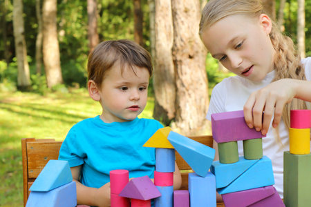 A girl plays with a small boy in colorful cubes in nature in summer in sunny weather.の写真素材