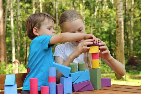 A girl plays with a small boy in colorful cubes in nature in summer in sunny weather.の写真素材