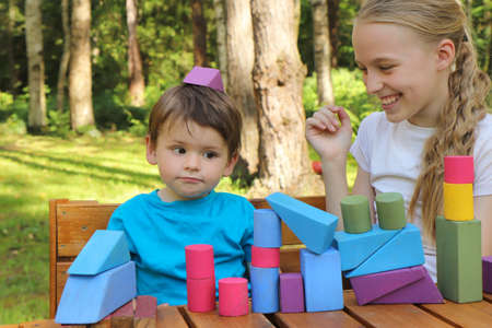 A girl plays with a small boy in colorful cubes in nature in summer in sunny weather.の写真素材