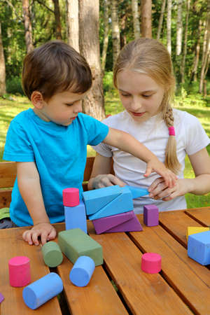 A girl plays with a small boy in colorful cubes in nature in summer in sunny weather.の写真素材