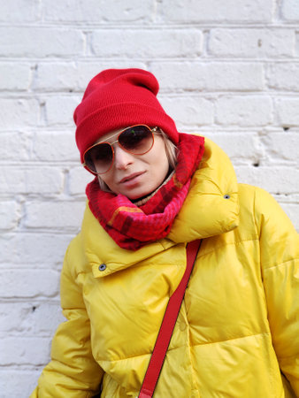 Young woman in a red-yellow fashionable image in sunglasses on a background of a white brick wall.の写真素材