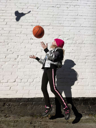 A sporty girl plays with a basketball against the background of a white brick wall with the shadow of a bird.の写真素材