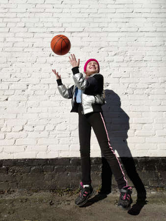 A sporty girl plays with a basketball against the background of a white brick wall with the shadow of a bird.の写真素材
