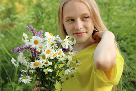 A blonde girl holding a bouquet of daisies in her hands on the background of nature.の写真素材