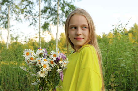 A blonde girl holding a bouquet of daisies in her hands on the background of nature.の写真素材