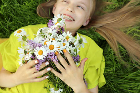 A blonde girl holding a bouquet of daisies in her hands lying on the green grass.の写真素材