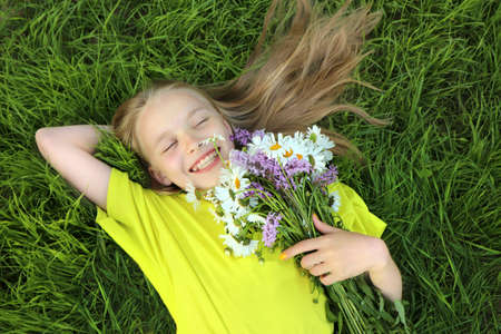 A blonde girl holding a bouquet of daisies in her hands lying on the green grass.の写真素材