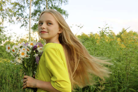 A blonde girl holding a bouquet of daisies in her hands on the background of nature.の写真素材